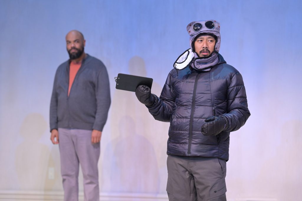 David Ryan Smith (Edmund) and Jomar Tagatac (Bob) in Berkeley Rep’s production of Charles L. Mee’s Wintertime, directed by Les Waters. The two actors stand on stage, one in a winter coat.
