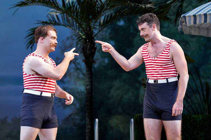 Two male opera singers, dressed in 1910s bathing costumes pointing fingers at each other