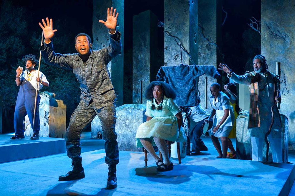 a man wearing a military uniform stands in the foreground with his arms up in the air and a surprised look on his face. A woman sits in a chair behind him. Stage shot from black odyssey