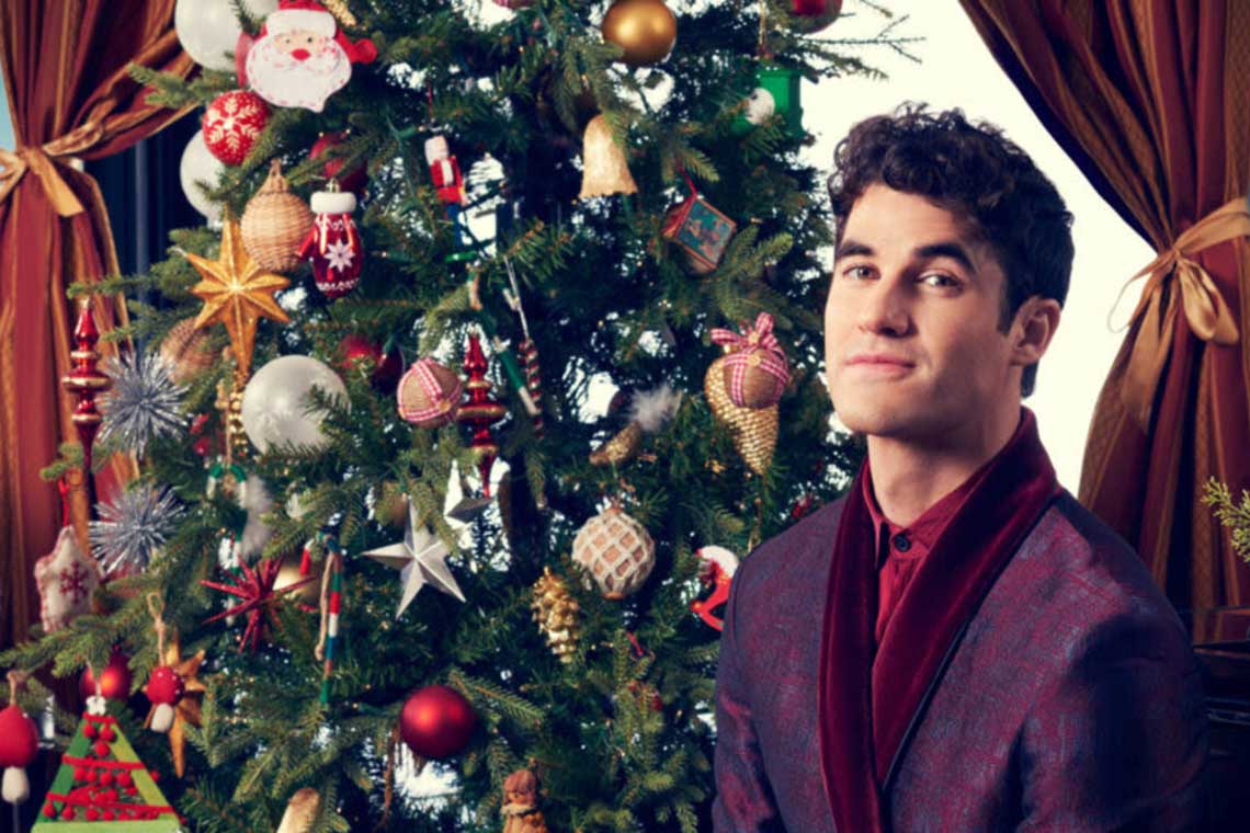actor and singer darren chriss stands in front of a christmas tree