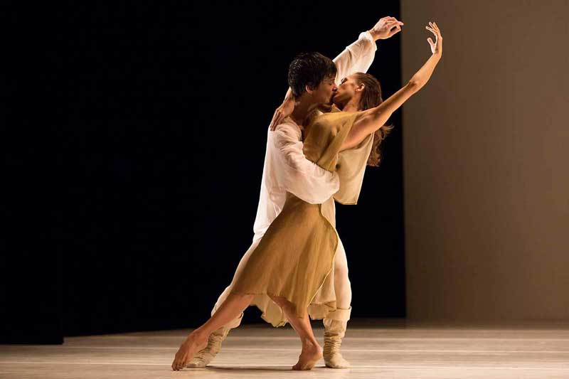a stage image of romeo and juliet. the two ballet dancers intertwine with one arm above their heads