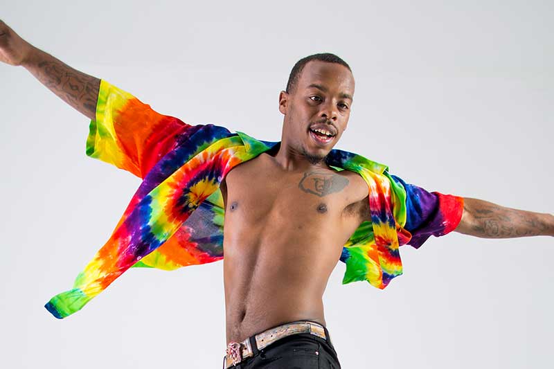 a Black man dances with his arms out stretched wearing a tie dye button down shirt