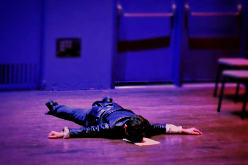 a teenage boy lies face down on stage during a play reading
