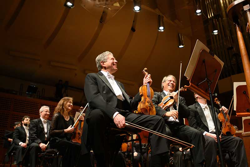 a group of orchestra players sit laughing