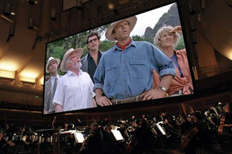 audience sits watching Jurassic park on a large screen above an orchestra