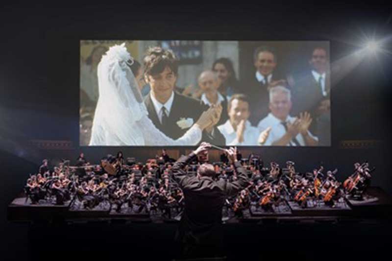 an audience sits and watches the godfather on a screen with an orchestra playing below