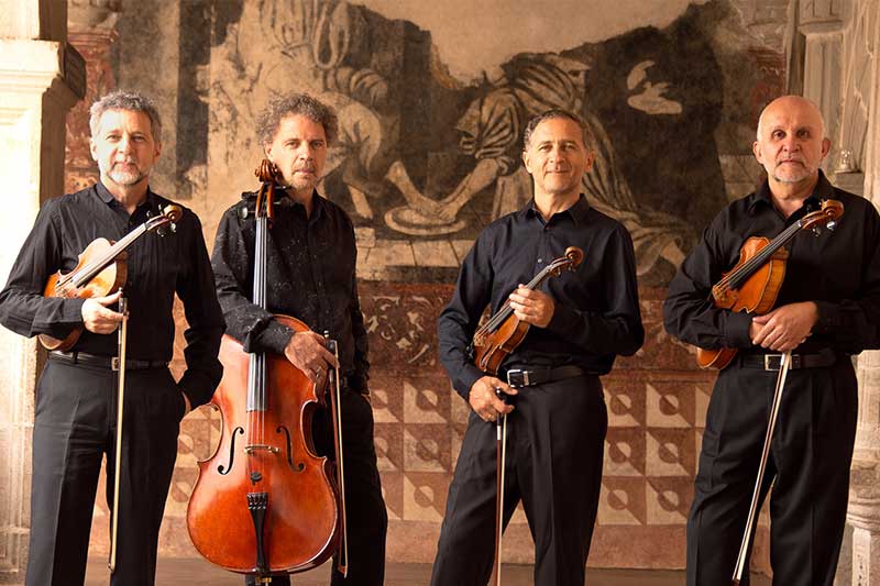 a quartet of musicians stands wearing black with instruments