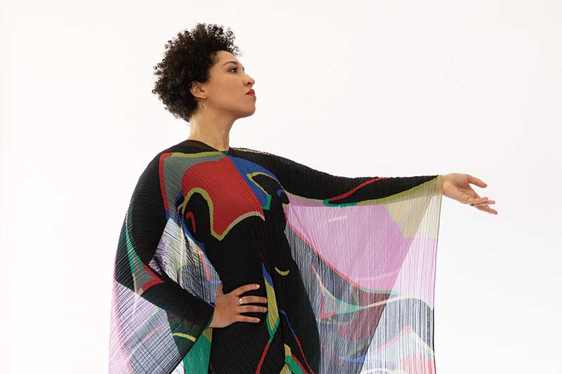 a black woman in a flowing geometric dress extends hand in a pose