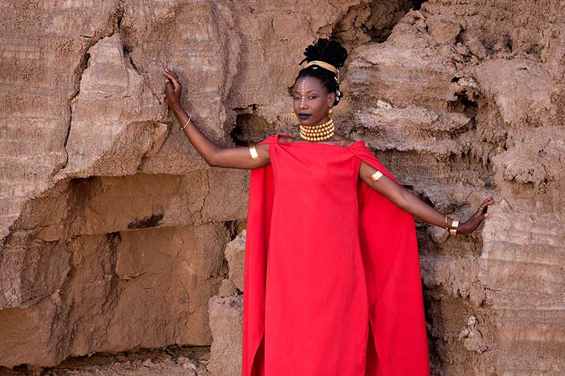 the artist fatoumata diawara stands in front of a rock wall in a long red dress