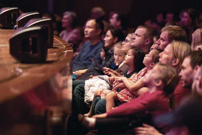an audience of parents sit watching something onstage with their children