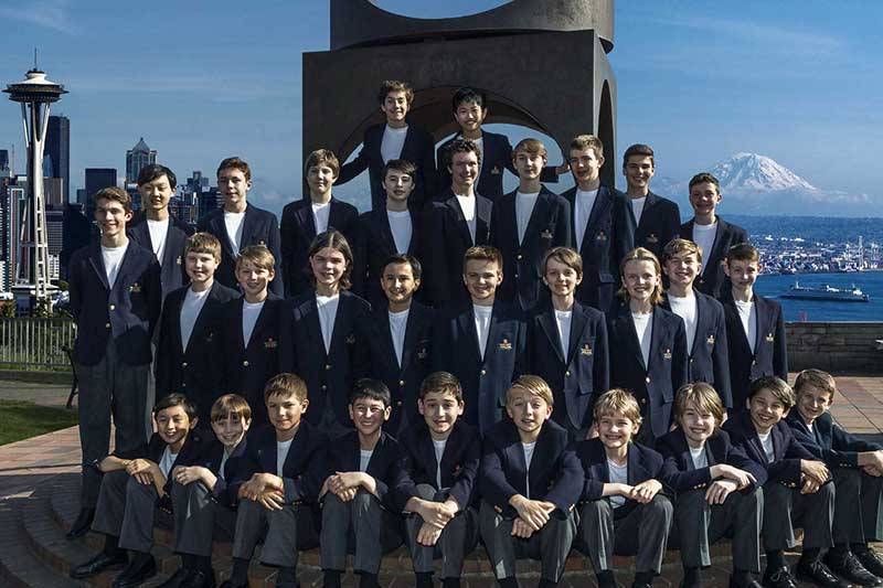the northwest boychoir sits outside with the space needle and a mountain in the background