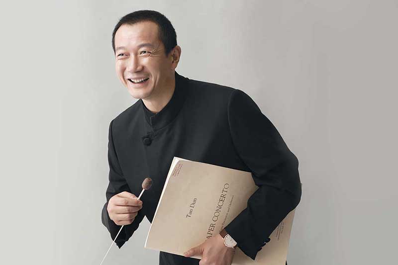press image of composer Tan Dun smiling and holding sheet music