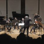 a musical group performs on stage in front of an audience with a conductor in front