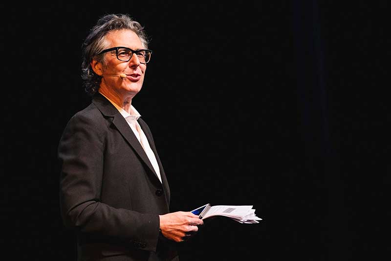 Ira Glass holds papers in his hand making a speech
