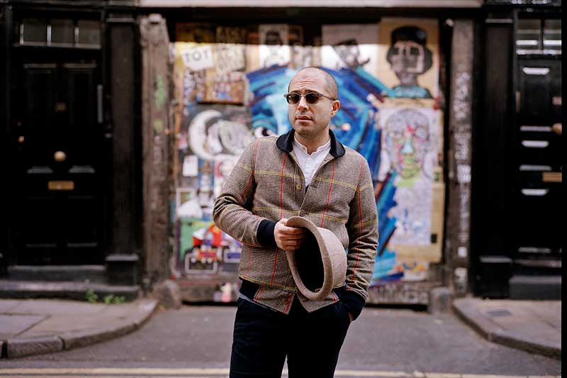 harpsichordist Mahan Esfahani stands outside in the city holding his hat