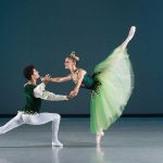 a man and woman ballet dancers in green. the ballerina has her leg high in the air dancing with the man