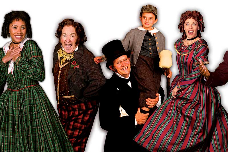 Promotional photo for "A Christmas Carol". A group of people dress in 19th century clothing smiling
