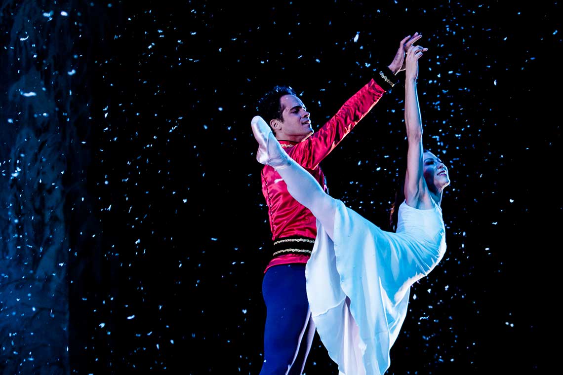 On stage, two ballet dancers dance together as snow falls around them. One is dressed as the prince and the other as clara from "The Nutracker."