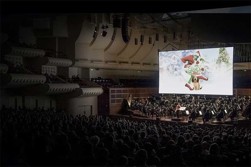 an audience watches how the grinch stole christmas on a large screen while the symphony plays