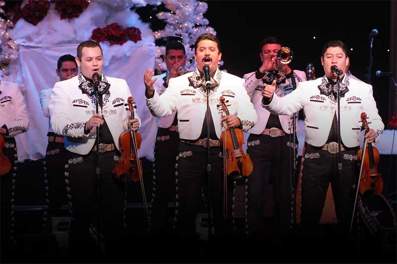 a mariachi band stands playing their instruments in white coats