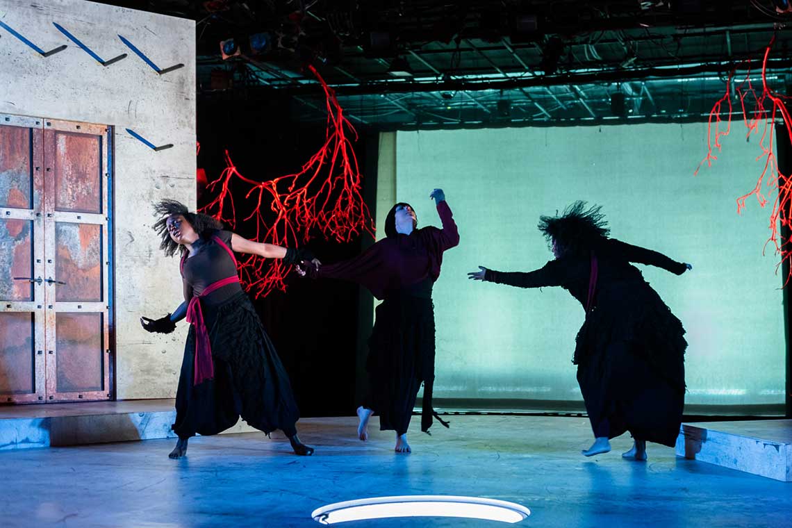 three women dressed in black dance wildly around a dark stage