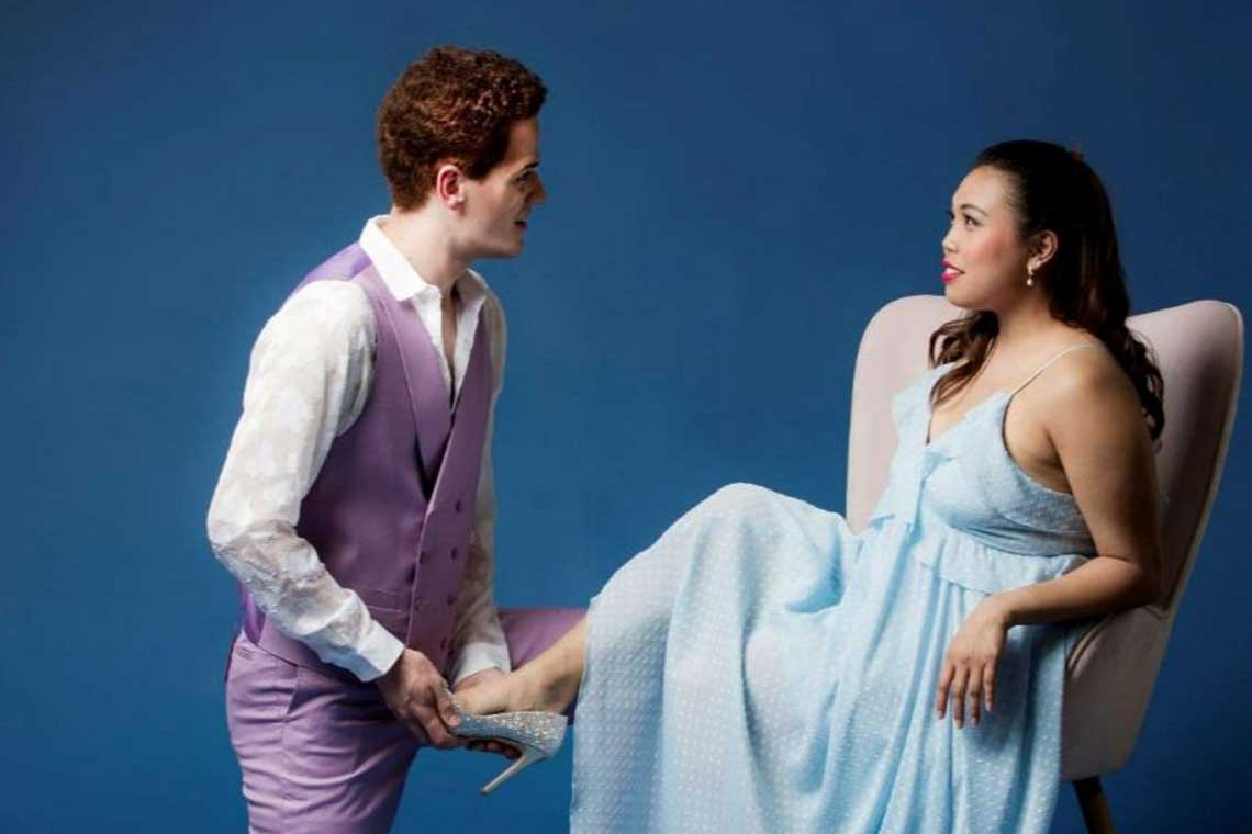 a man in a purple suit kneels in front of a woman in a blue dress and puts a shoe on her foot