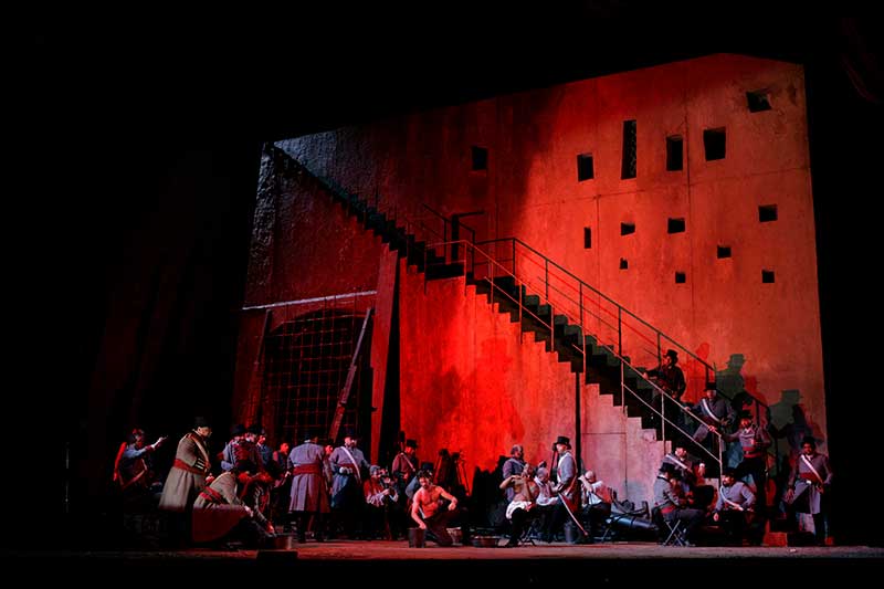 On stage a dark red light shows a castle like background with 20 people in front of it.