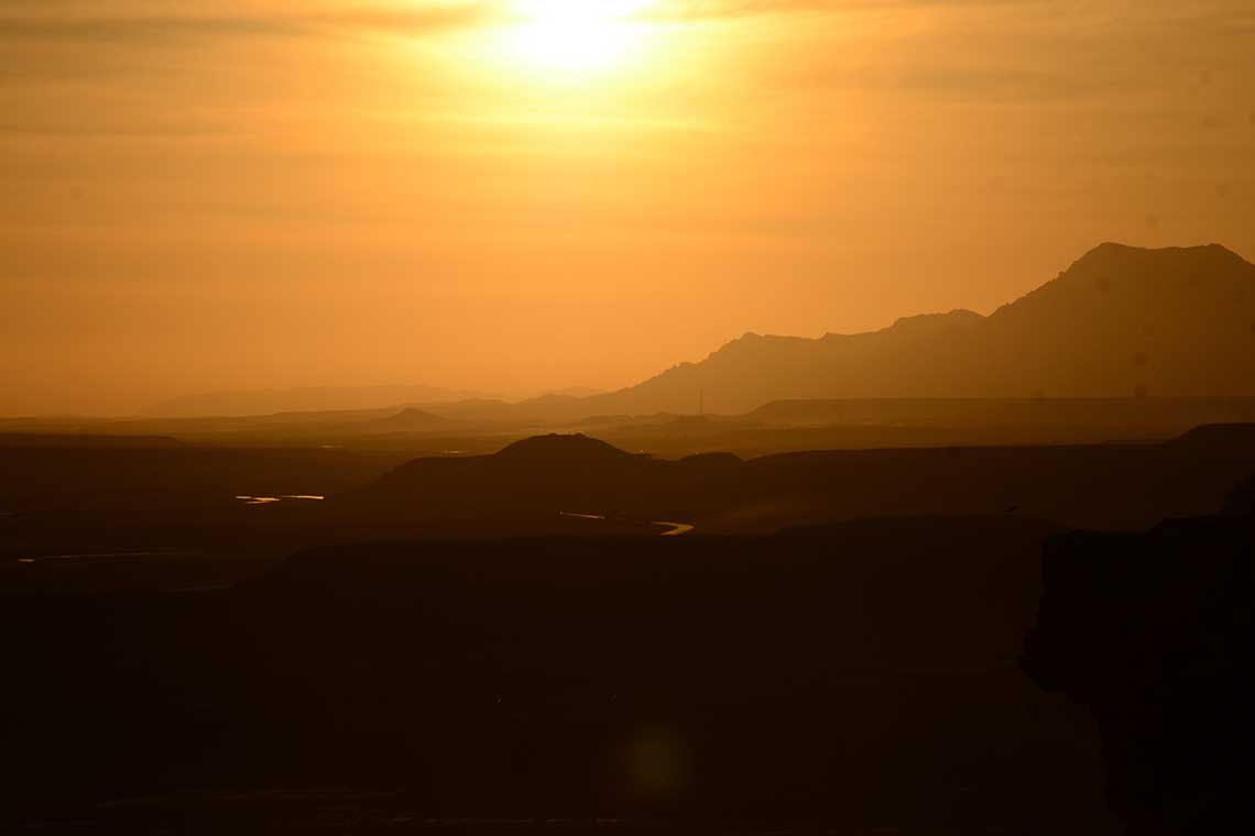 A sunrise over some desert mountains gives a yellow light to the landscape.