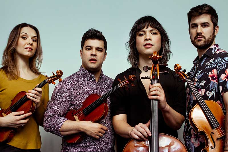 Two men and two women stand holding their string instruments.