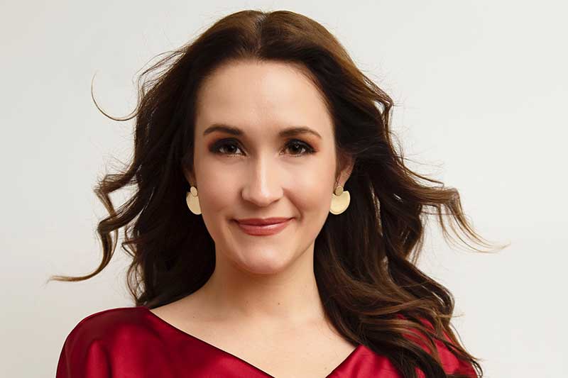 A white woman with brown hair wears a red shirt.