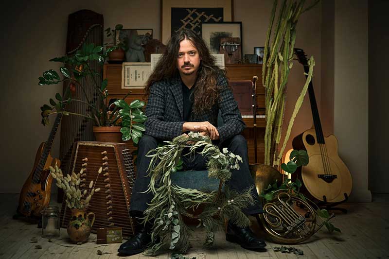 A white man sits surrounded by plants and instruments.