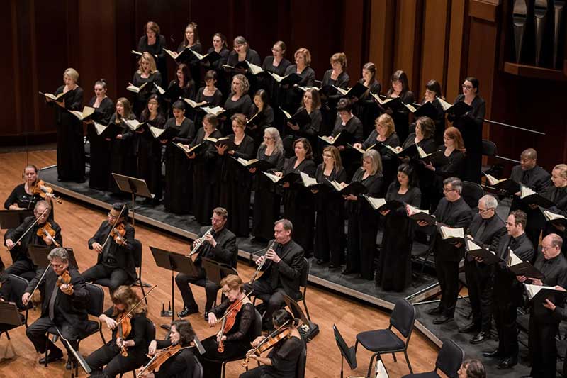 Seattle Symphony choir members wear black robes and sing.