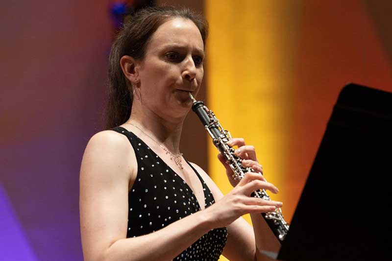 A white woman with her hair in a ponytail plays the oboe.
