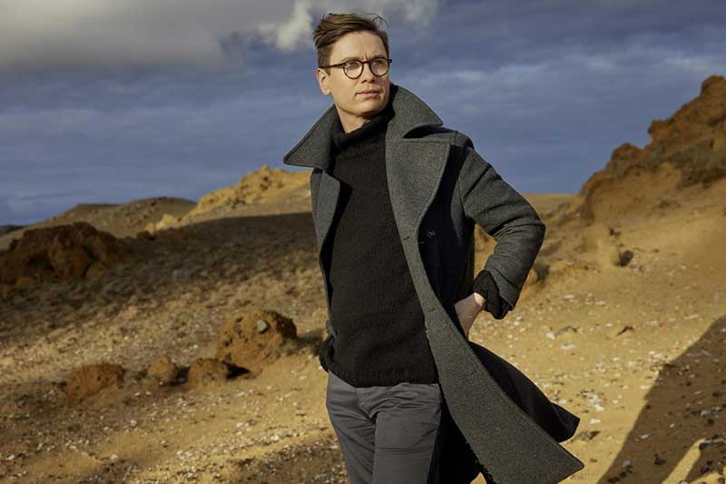 A white man with glasses stands in front of a desert background