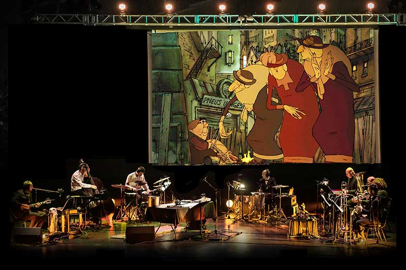 A group of musicians play on stage with a large film playing behind them.