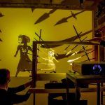 on a yellow background, puppeteers work with shadow and light.