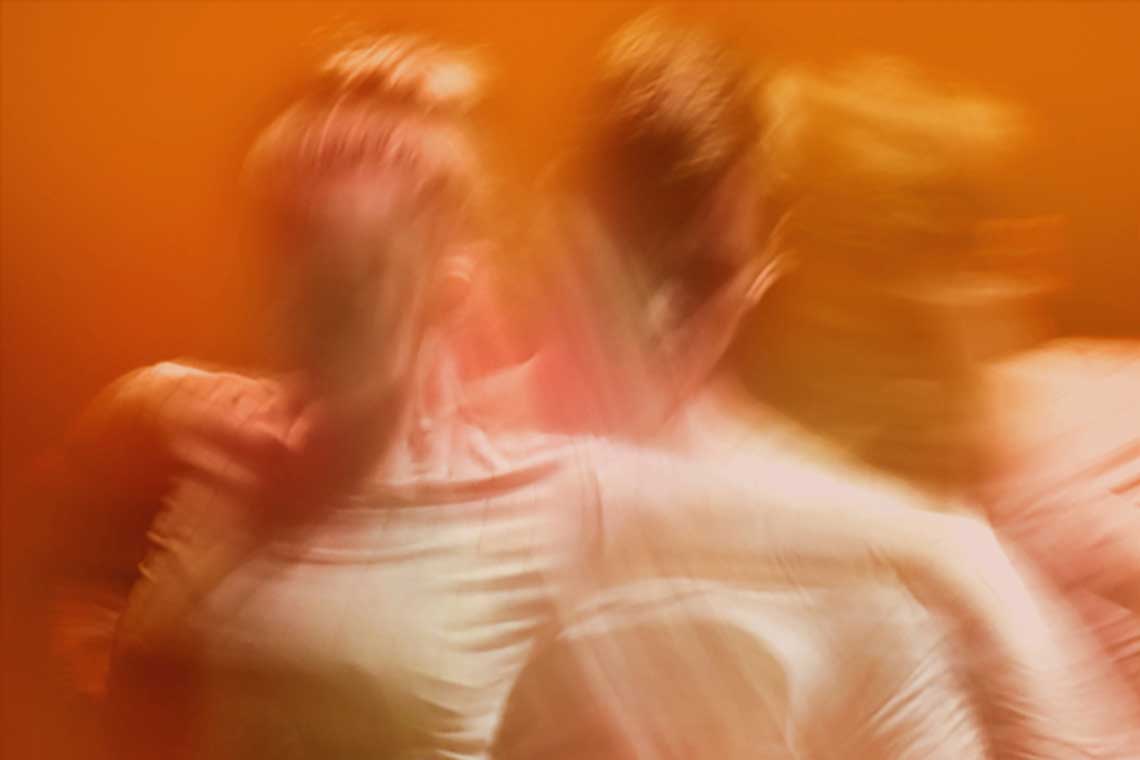 A blurry image of two dancers in front of an orange background.