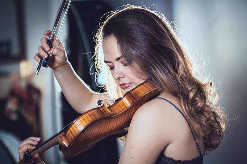 A young woman with brown hair plays the violin.