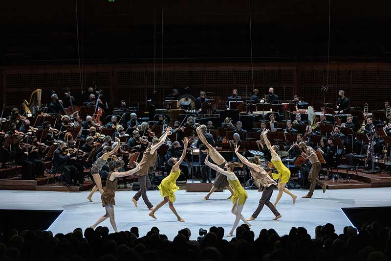 A ballet company wearing yellow dances on stage.