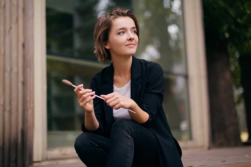 A young white woman with short brown hair crouches down hold a conductors baton.