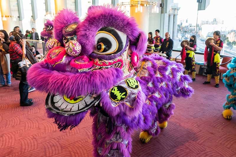 A large purple Chinese dragon is paraded in the lobby of a building with people watching.