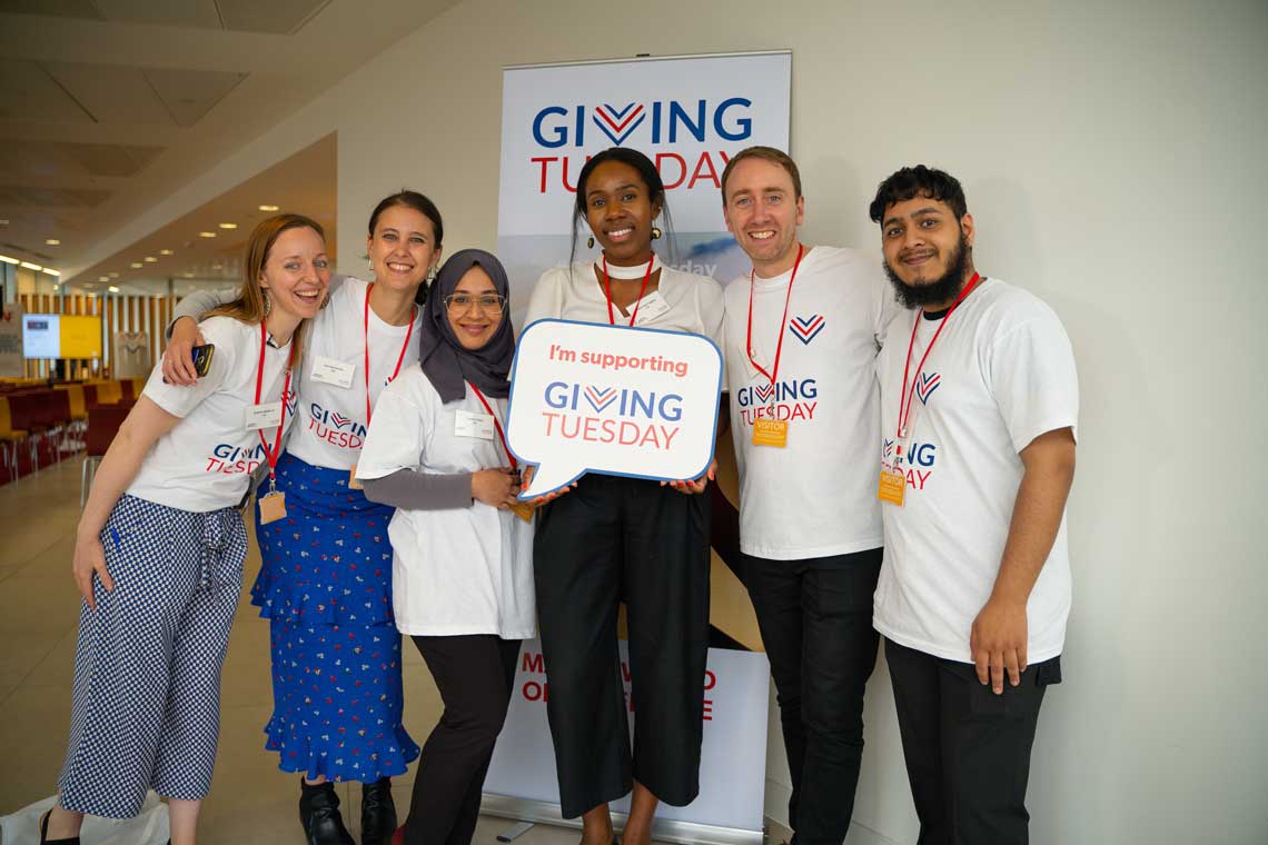 A group of young people stand together holding a sign for GivingTuesday.