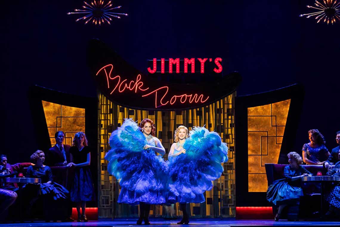 On stage, two women dressed in fancy blue dresses dance with their skirts flying around.