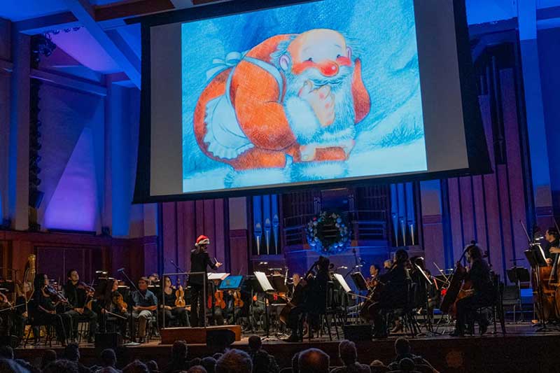 Seattle Symphony plays on stage with The Snowman film playing behind them.