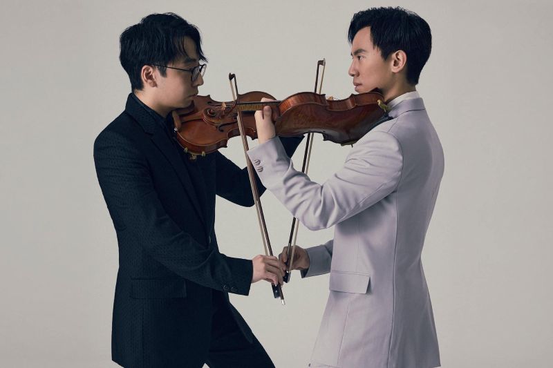 Two violinists play their instruments facing each other.