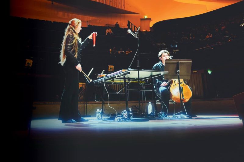 A woman and man play music on stage with a spotlight on them.