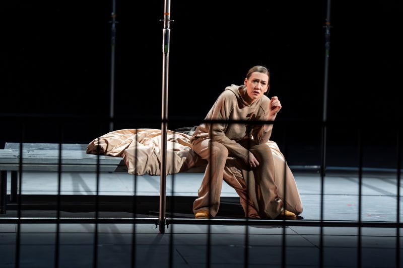 A woman sits on a cot in a jail.