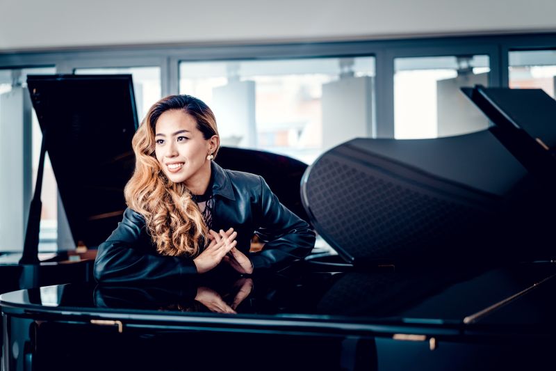Janice Carissa sits at a grand piano.