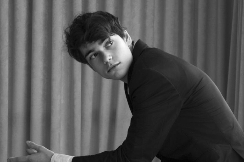 Black and white photo of Tom Borrow sitting down with his arms on his knees looking off camera.